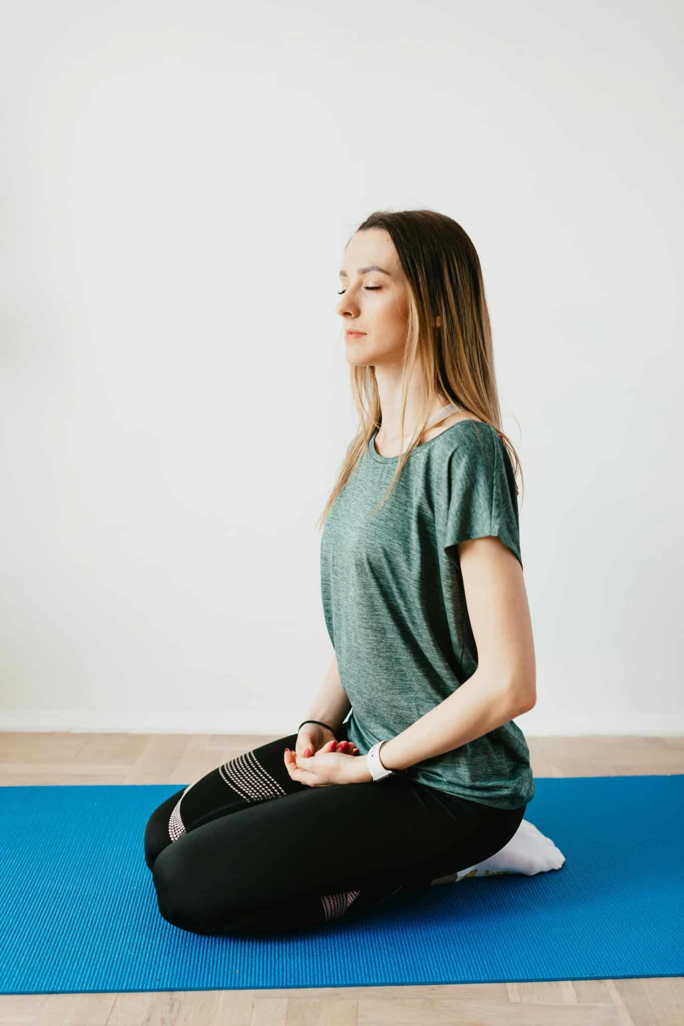 Side view of young slim female in sportswear sitting in Virasana pose with closed eyes while practicing yoga at home