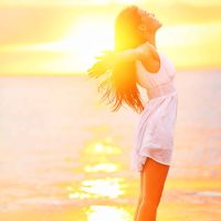 Free woman enjoying freedom feeling happy at beach at sunset. Beautiful serene relaxing woman in pure happiness and elated enjoyment with arms raised outstretched up. Asian Caucasian female model.