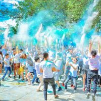 Energetic crowd enjoying a vibrant outdoor festival with colorful powder at daytime.